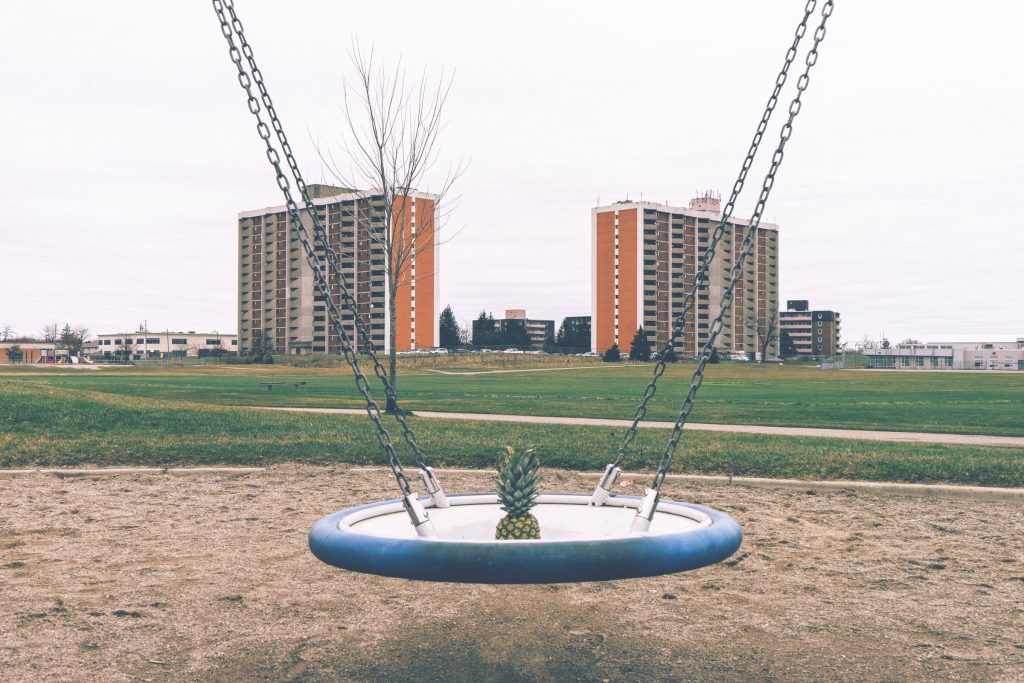 A single swing in an open field with tower blocks behind it