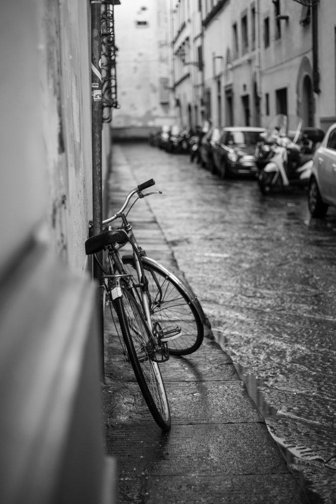A narrow street in the rain, a bicycle chained to a wall